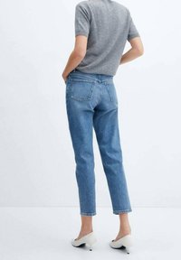 Fitted blue jeans with a straight cut, five pockets, and a mid-rise waist, paired with a gray short-sleeve top and white heels.