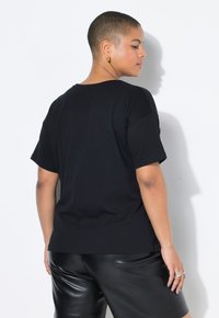 Černé tričko s krátkým rukávem vyrobené z bavlny, s uvolněným střihem a jemnou texturou. V kombinaci se lesklými černými kalhotami.