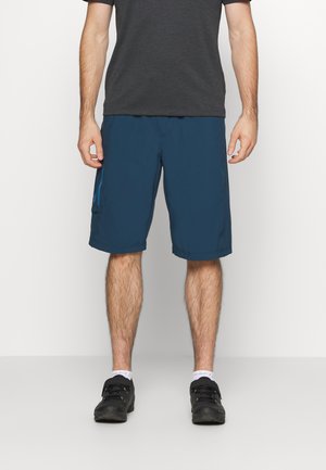Men's blue shorts with an elastic waistband, side pockets, and a smooth, lightweight fabric. Model is wearing black shoes.