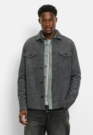 Gray wool jacket with a collar, two chest pockets, and black snap buttons, layered over a light green shirt. Textured fabric with a casual fit.