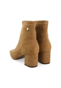 Bottes à cheville en daim tan avec un bout pointu, un talon bloc et des détails de couture subtils. Accent métallique à l'arrière pour un design supplémentaire.