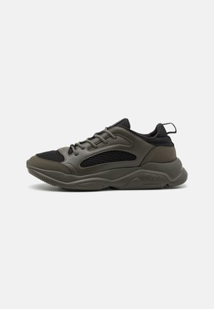 Sneaker con lacci in una costruzione in rete verde scuro e nera, dotati di collo imbottito, suola testurizzata e accento con logo sul lato.
