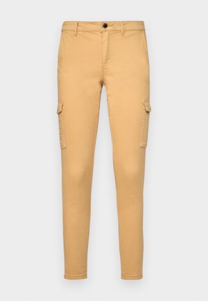 Pantalones cargo beige de tela de algodón, con bolsillos laterales, cierre de botón en la parte delantera y un diseño de corte ajustado. Textura suave, sin patrones visibles.