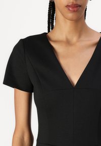Black dress with short sleeves, V-neck design, structured bodice, and subtle seams. Smooth fabric texture with a fitted silhouette.