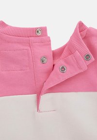 Polo en coton rose et blanc avec col à snap, présentant un motif tricoté texturé et une petite poche sur le côté supérieur gauche.