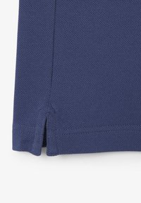 Polo de color azul marino con tejido texturizado, ligeras aberturas laterales en el dobladillo y costuras reforzadas para mayor durabilidad.