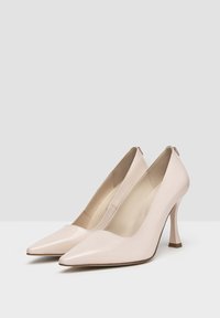 Pale pink patent leather high heels with pointed toes and a curved heel design. Smooth texture with a minimalistic interior lining.