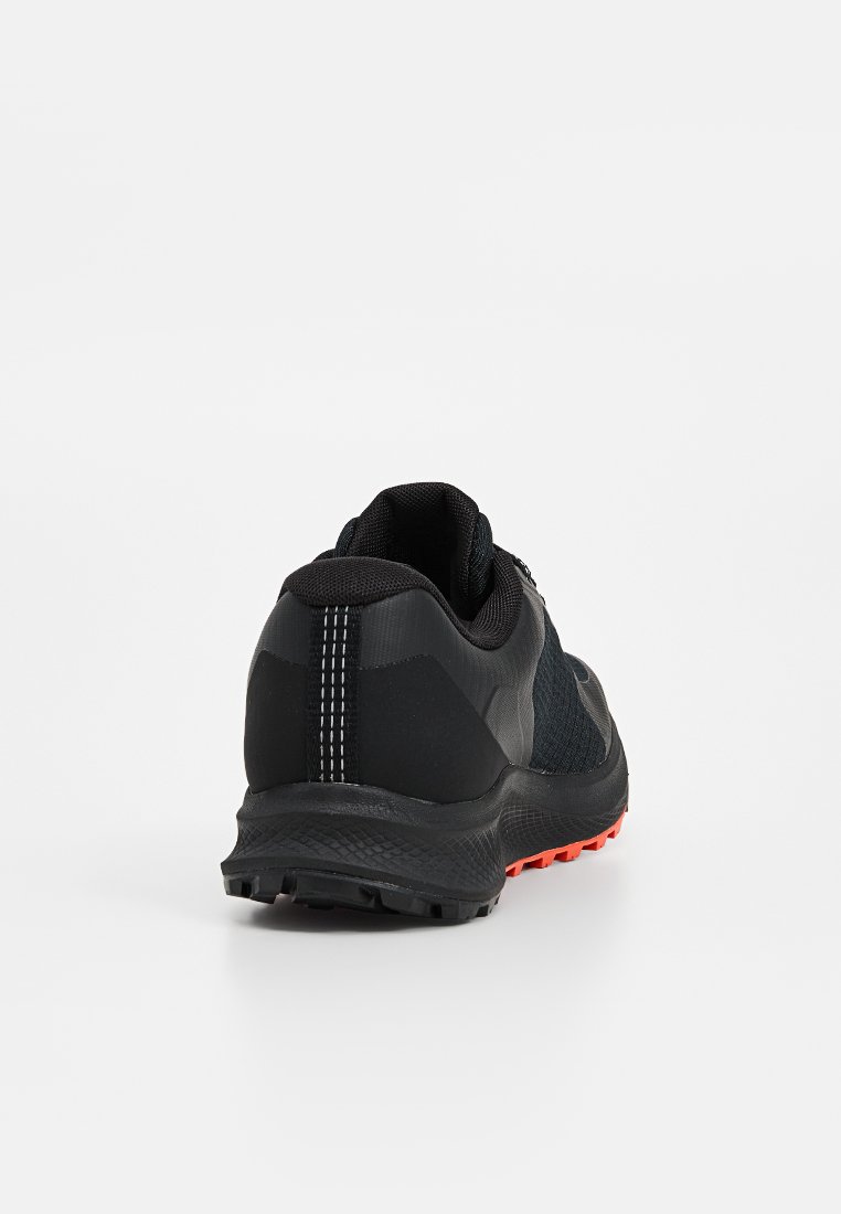 Chaussure de sport noire en mesh et matériau synthétique, avec un talon texturé, une semelle extérieure orange contrastante et des accents de coutures blanches.