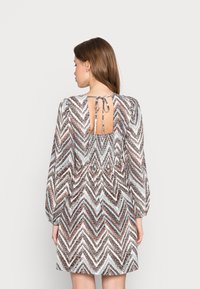 Vestido de mangas curtas com padrão em zigzag nas cores castanho, azul e branco. Costas abertas com fecho de laço; tecido suave e corte relaxado.