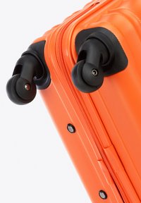 Valise rigide de couleur orange vif, dotée d'une finition texturée, de roues noires encastrées et d'une fermeture éclair lisse sur le côté.