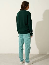 Groene wollen trui met een ontspannen pasvorm, gecombineerd met lichtgroene gestreepte ribfluwelen broek. Witte sneakers maken de outfit compleet.
