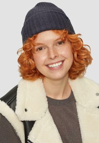 Navy ribbed knit beanie, soft texture; worn by a person with shoulder-length curly orange hair, paired with a cream faux shearling jacket.