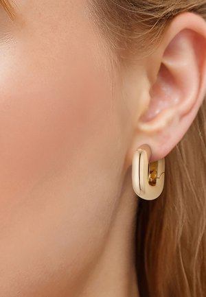 Goldener Creolen-Ohrring mit polierter Oberfläche, der ein geschwungenes, massives Design aufweist. Mit einem Scharnierverschluss befestigt, hängt er am Ohrläppchen.