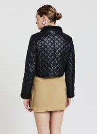 Veste en simili cuir matelassé noir avec un col, design court et manches longues. Associée à une mini jupe beige avec des poches sur les côtés.