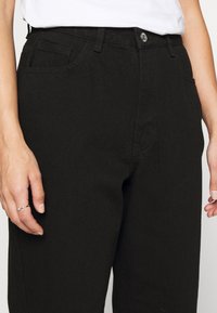 Pantalones de mezclilla negros con un diseño clásico de cinco bolsillos, corte recto, costuras visibles y un cierre de botón plateado en la cintura.