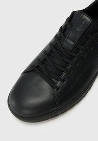 Sorte lær sneakers med flate lisser, rund tå og teksturert overflate. Har en lavprofil gummisåle og minimal merkevaredetalj.