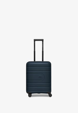 Valigia rigida di un profondo blu navy, caratterizzata da scanalature orizzontali, un logo centrale, un manico estensibile nero e quattro ruote nere per la mobilità.