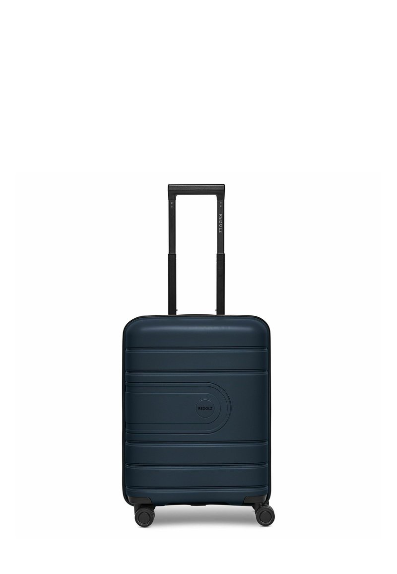 Harde koffer in diep marineblauw, met horizontale groeven, een centraal logo, uitschuifbare zwarte handgreep en vier zwarte wielen voor mobiliteit.