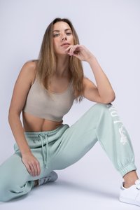 Svetlo béžový rebrovaný crop top v kombinácii s mätovo zelenými teplákmi s bielym potlačou na strane, doplnené bielymi teniskami.