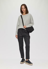 Lichtgrijze sweatshirt en zwarte geblokte broek, gecombineerd met chunky zwarte sneakers. Accessoires omvatten een zwarte schoudertas.