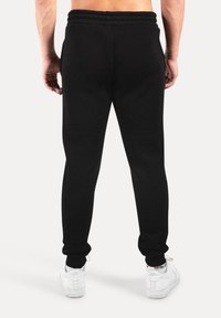 Sorte joggingbukser med elastisk talje og manchetter, der har en glat tekstur. Båret med hvide sneakers og viser et slankt fit design.