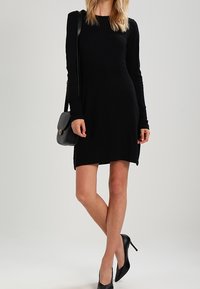 Černé šaty s dlouhým rukávem a ribovanou texturou, slim fit, do kolen. Nosené s kabelkou přes tělo a černými lodičkami na vysokém podpatku.