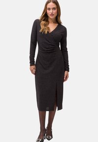 Schwarzes, langärmliges Kleid mit Wickeldesign, aus strukturiertem Stoff, seitlichem Schlitz und mittellanger Länge bis zur Wade. Mit subtiler Glanzakzenten.