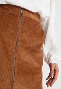 Gonna in velluto corduroy marrone con righe verticali, dotata di zip laterale. Il tessuto ha una consistenza morbida e un design aderente.
