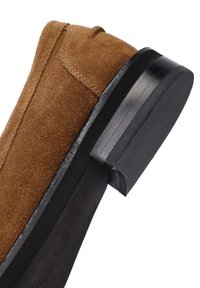 Chaussure en daim brun avec une semelle en cuir noir lisse. Présente un bout arrondi, des détails de couture subtils et un talon incliné pour la stabilité.