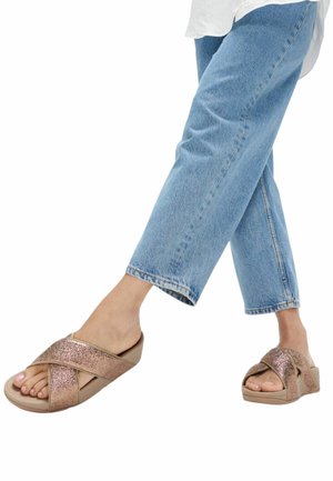 Bronzen sandalen met gekruiste bandjes, een gestructureerde afwerking, een platte zool en een gewatteerd voetbed, gecombineerd met lichtblauwe jeans met rechte pijpen.