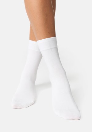 Chaussettes de cheville en coton blanc avec une bordure côtelée, texture lisse et design sans couture au niveau des orteils, présentées sur une jambe partiellement visible.