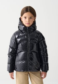 Melnā pūkaina jaka ar spīdīgu apdari, augstu apkakli, rāvējslēdzēja aizdari un elastīgām manšetēm. Gluda tekstūra un izšūts raksts.