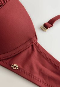 Sutien cărămiziu realizat din material neted, cu cupe modelate, bretea ajustabilă și accesorii aurii. Se observă detalii de cusături.