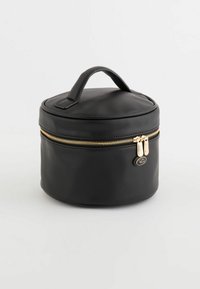 Round black cosmetic bag with a textured surface, gold zipper, and a top handle for easy carrying. Features a small branded accent tag.