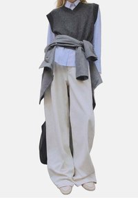 Graue gestrickte Weste über einem hellblau gestreiften Hemd, kombiniert mit beigen Hosen mit weitem Bein und einem grauen Pullover, der an der Taille gebunden ist.