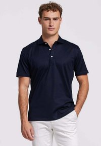 Marineblauwe polo shirt van gladde stof, met een klassieke kraag, een drie-knopen sluiting en korte mouwen. Draagt met witte broek.