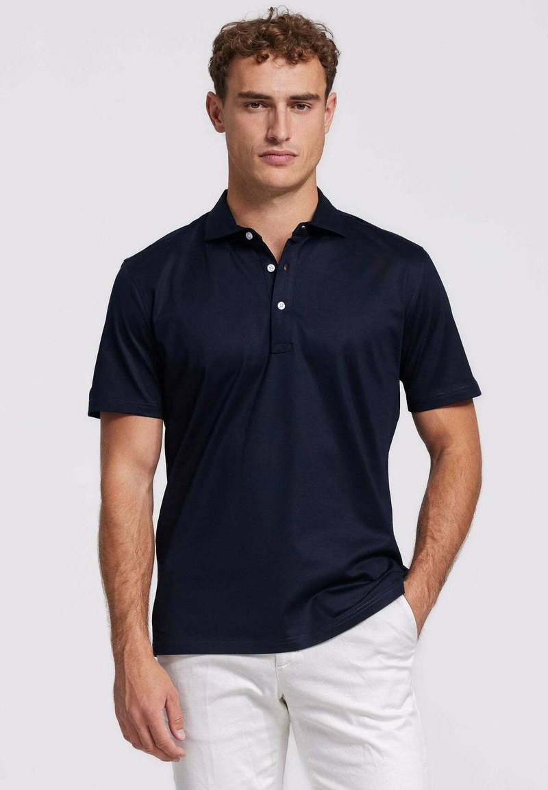 Marineblauwe polo shirt van gladde stof, met een klassieke kraag, een drie-knopen sluiting en korte mouwen. Draagt met witte broek.