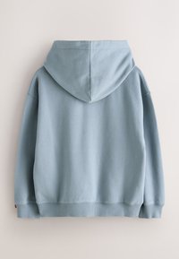 Hele sini kapuutsiga dressipluus, valmistatud pehmest kangast, millel on tekstuurse viimistlusega pinnakate. Omadused: keskmine tagumine õmblus ning soonilised mansetid ja alumine äär.