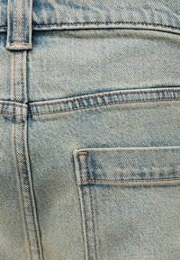 Κοντινό πλάνο ανοιχτό μπλε τζιν παντελονιού που δείχνει την πίσω τσέπη και το λουράκι της ζώνης με εμφανείς λεπτομέρειες ραφής.