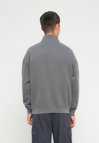 Sudadera gris con un cuello alto, puños y dobladillo acanalados, hecha de una tela suave. La vista desde atrás muestra un ajuste relajado y detalles de diseño mínimos.