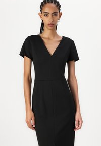Black fitted dress with short sleeves, deep V-neckline, and structured panels. Smooth fabric, knee-length, minimalistic design details.