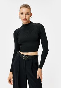 Top corto nero a costine con maniche lunghe e collo alto, abbinato a pantaloni a vita alta e una cintura nera con una fibbia circolare.