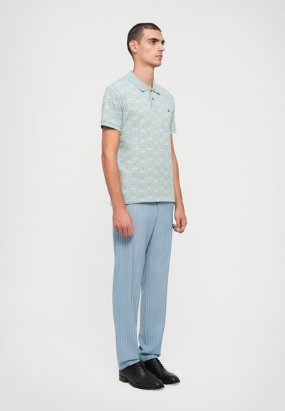 Polo de culoare albastru deschis cu un model subtil, asortat cu pantaloni dungi cu dungi albastre deschise și pantofi negri. Țesătură fină, croială clasică.