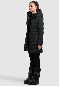 Čierny prešívaný kabát s kapucňou, vertikálnym prešívaním, predným zipsom a bočnými vreckami. Nosený s čiernymi elegantnými snehovými čižmami.