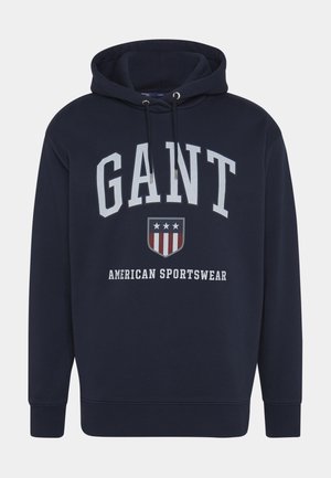 Donkerblauwe sweatshirt met capuchon, voorzien van witte "GANT" tekst en een schildlogo van de Amerikaanse vlag. Zachte stof, geribbelde manchetten en zoom.