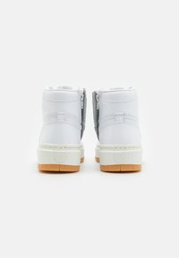 Baskets montantes avec une tige en cuir blanc, des accents en suede gris, fermeture éclair, et une épaisse semelle intermédiaire crème avec une semelle extérieure en caoutchouc beige.