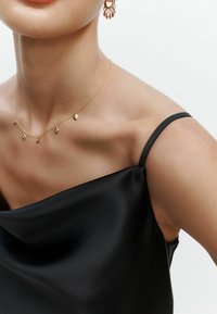 Mustat satiinimekko, jossa on olkaimeton muotoilu, jossa on sileä rakenne ja ohut hihna. Kulta ketjun kaulakoru, jossa on timantin muotoisia yksityiskohtia.