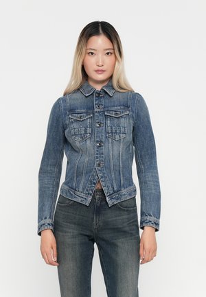 Jeansjack met een slim fit ontwerp, blauwe kleur, twee borstzakken, knoopsluiting en een licht rafelige zoom, gedragen over een donkere spijkerbroek.