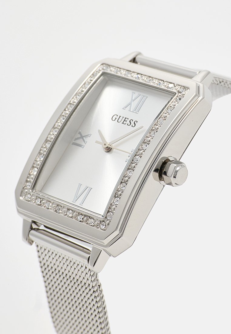 Reloj de pulsera rectangular Guess plateado con bisel incrustado de cristales, números romanos en la esfera, correa de malla plateada y tres agujas.