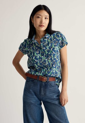 Kortærmet skjorte med krave i blå med grønne blomsterprint. Båret med højttaljede, løstsiddende denimjeans og et brunt bælte.